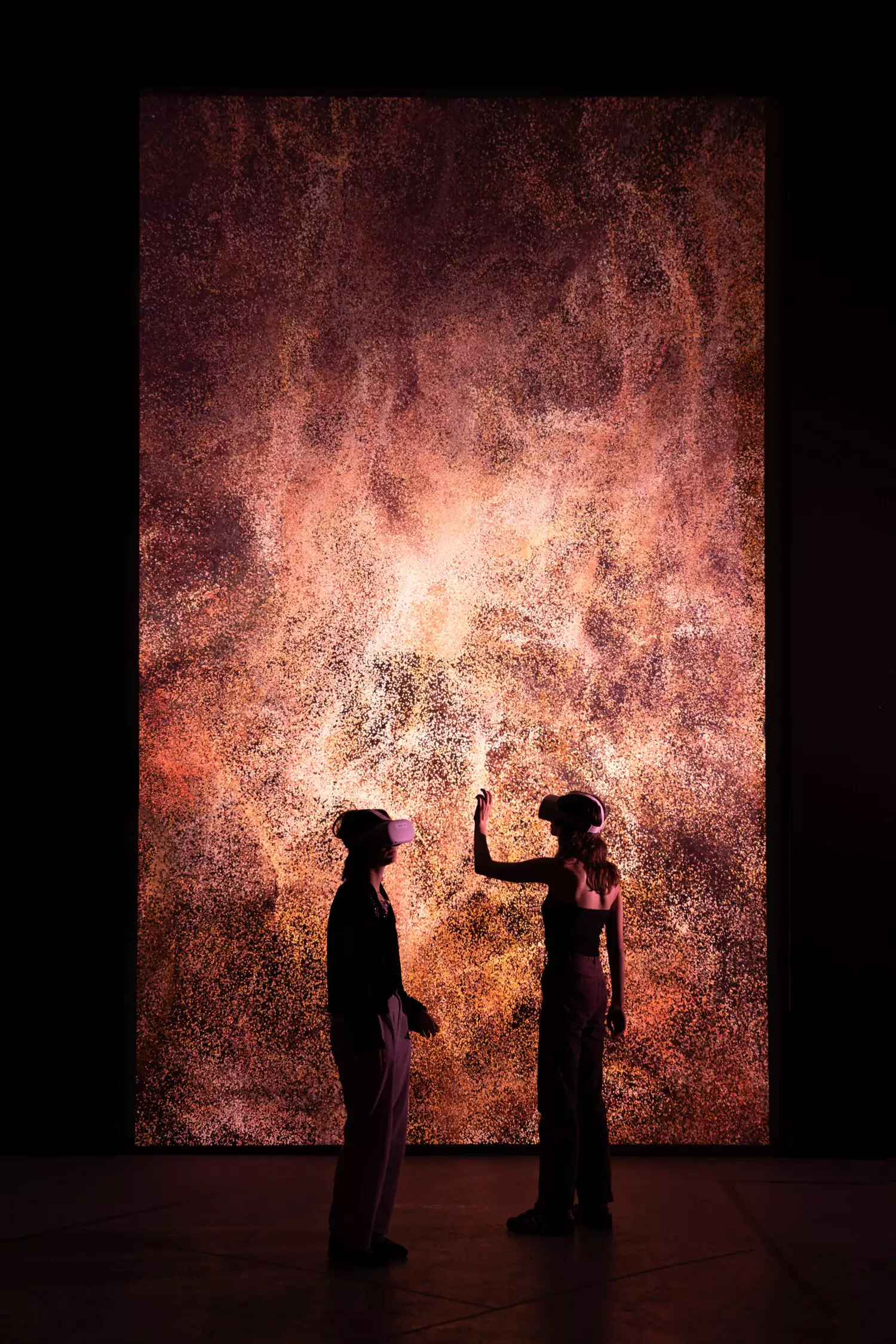 Two spectators wearing headsets experience a digital artwork on a large vertical screen