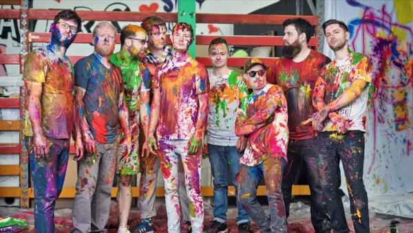 Nine members of Young Pilgrims covered in colourful paint, posing in an artistic setting.