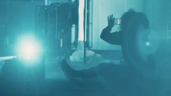 Juliet Ellis taking a photo sat on the floor, in a blue-lit, smoky environment.