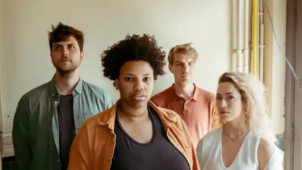 Four members of Nabou wearing clothes with muted colours stood in front of a cream wall. They are all looking in different directions.