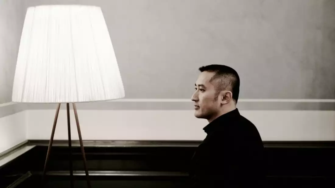 Huang Ruo looking to the side, posing next to a large white lamp
