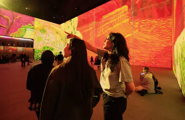 An image from David Hockney: Bigger & Closer (not smaller & further away) showing two people pointing upwards at the exhibition