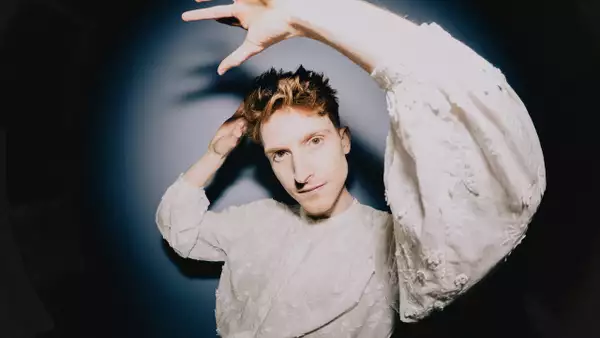 Bay Bryan wearing a white top lifting their hands in the air