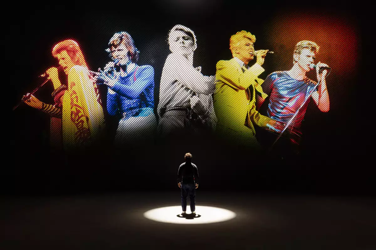 A person looking at five versions of David Bowie singing on a large screen