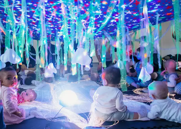 Babies sat under a large sheet with colourful stars and lights