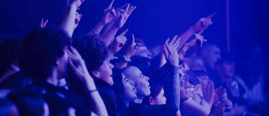 A crowd of people cheering and filming over the barrier in the Warehouse at Aviva Studios. The lighting is blue.