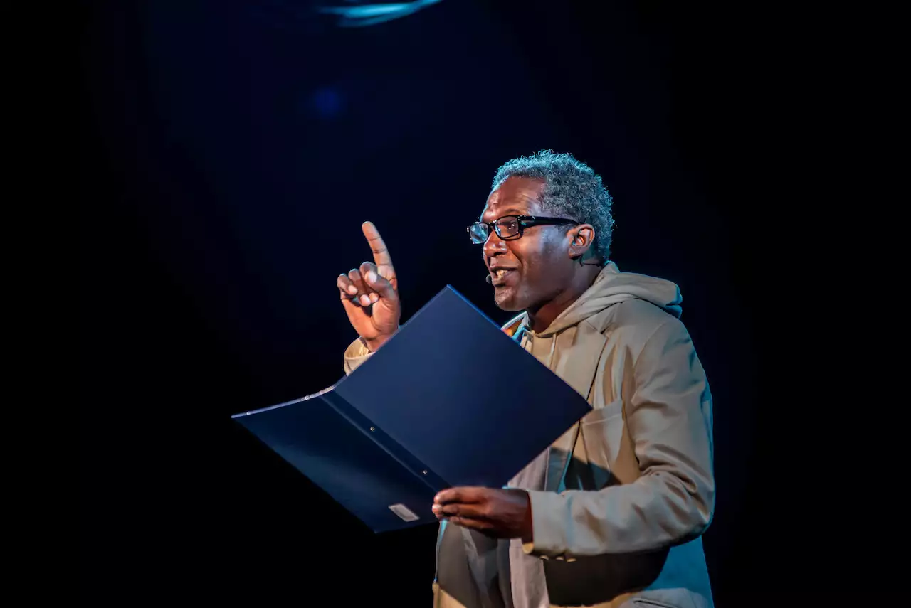Lemn Sissay reading from a folder, with his finger pointing in the air