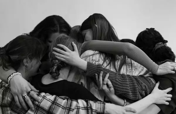 A black and white photograph of young people with their arms around each other in a group cuddle