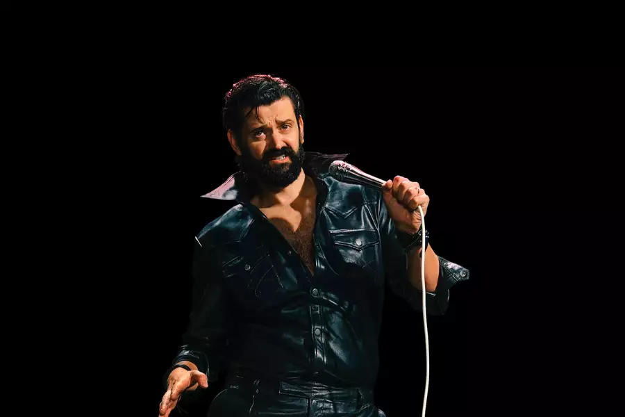 Fin Taylor wearing a black leather outfit and holding a microphone on a black background