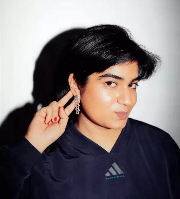 Areesha Ali wearing a black Adidas sweatshirt and silver earrings on a white background