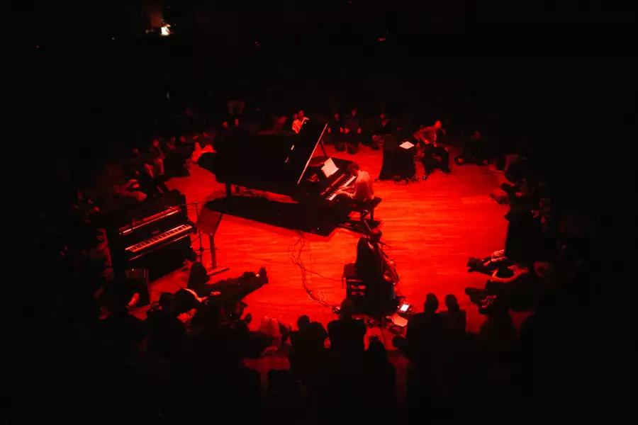 Jon Hopkins playing piano on stage with red lighting and instruments around him