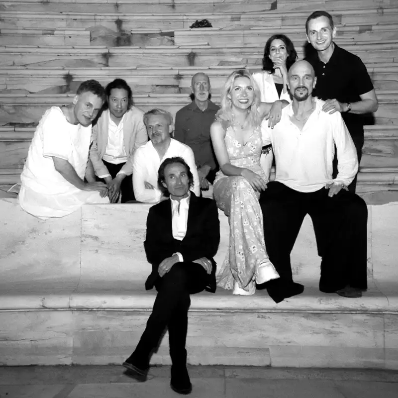 Nine members of James sitting and standing on stone steps. The image is black and white. They are casually dressed, some in light-colored clothes, with one person in a dress, and others in shirts or casual attire.