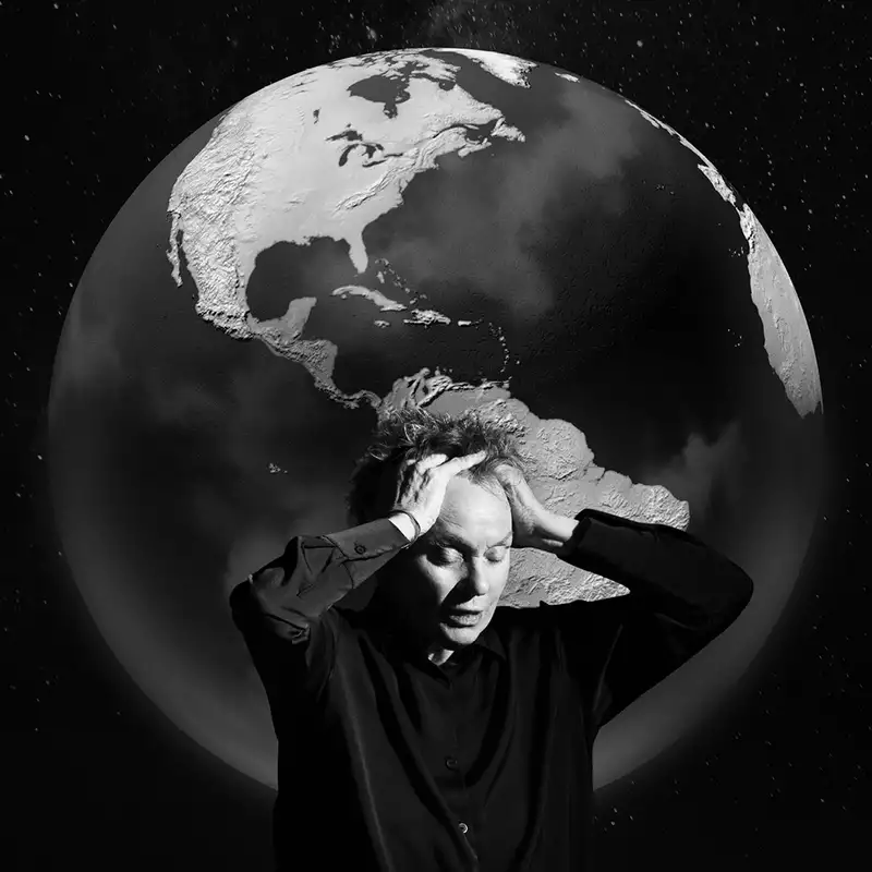 Black and white image of Laurie Anderson with her eyes closed and hands on her hand. Behind her is the earth.