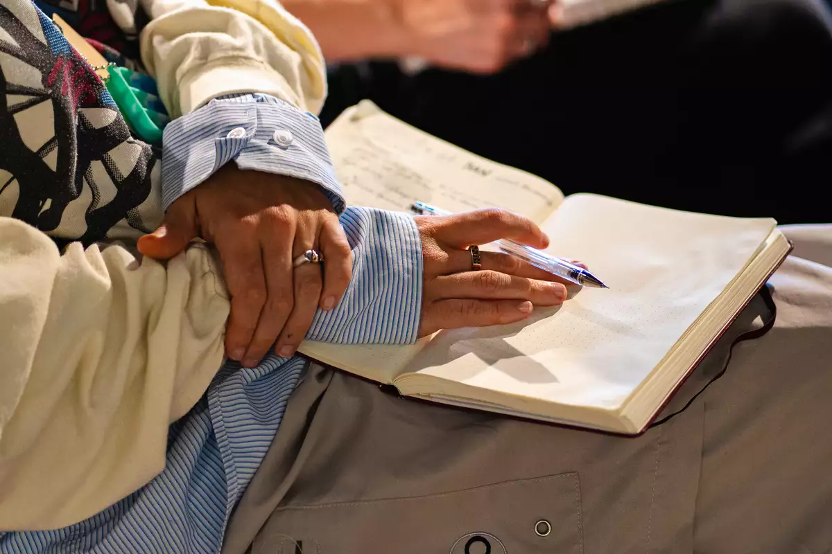 A close-up image of a person holding a pen and resting their hands on an open notebook.