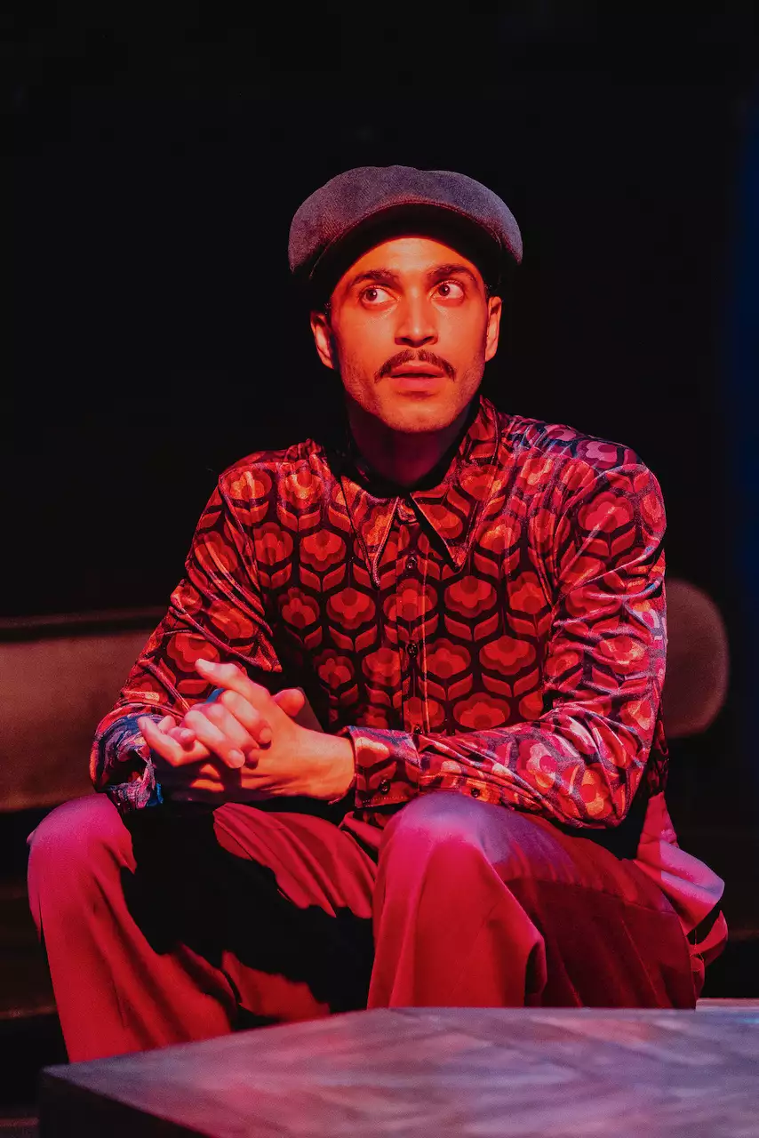 An actor wearing a hat, mid-speech, on stage during Liberation