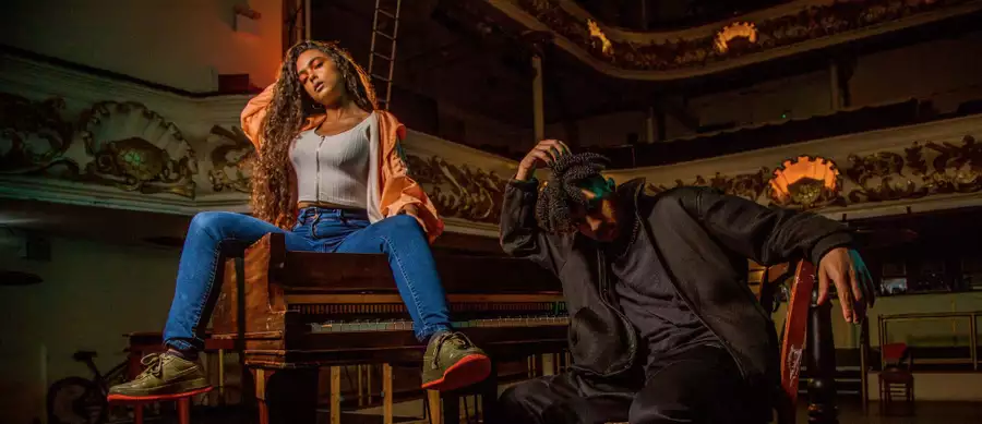 A photo of two people posing next to a grand piano in a concert hall