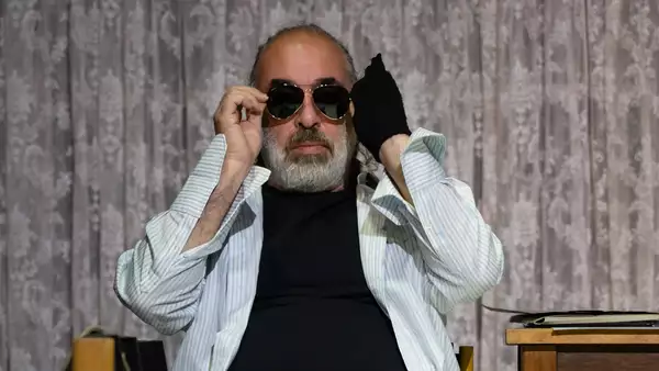 On stage, a man with sunglasses looks straight ahead