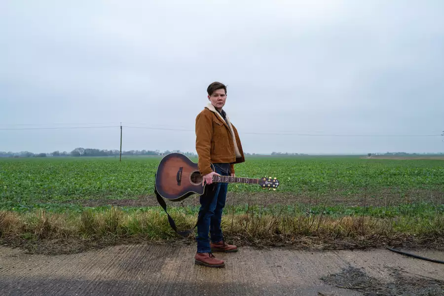 Grace Petrie stood in a field with a guitar
