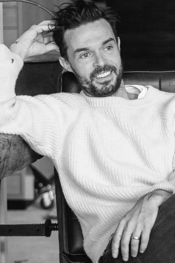 Black and white photo of Oliver Jeffers sat on a black leather chair