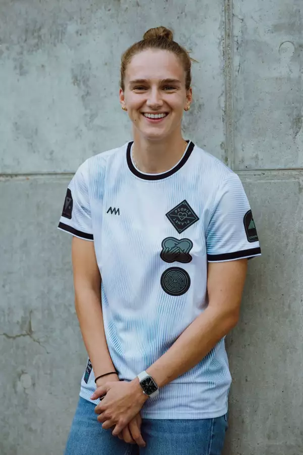 VIVIANNE MIEDEMA wearing a white football shirt stood in front of a grey background, smiling.