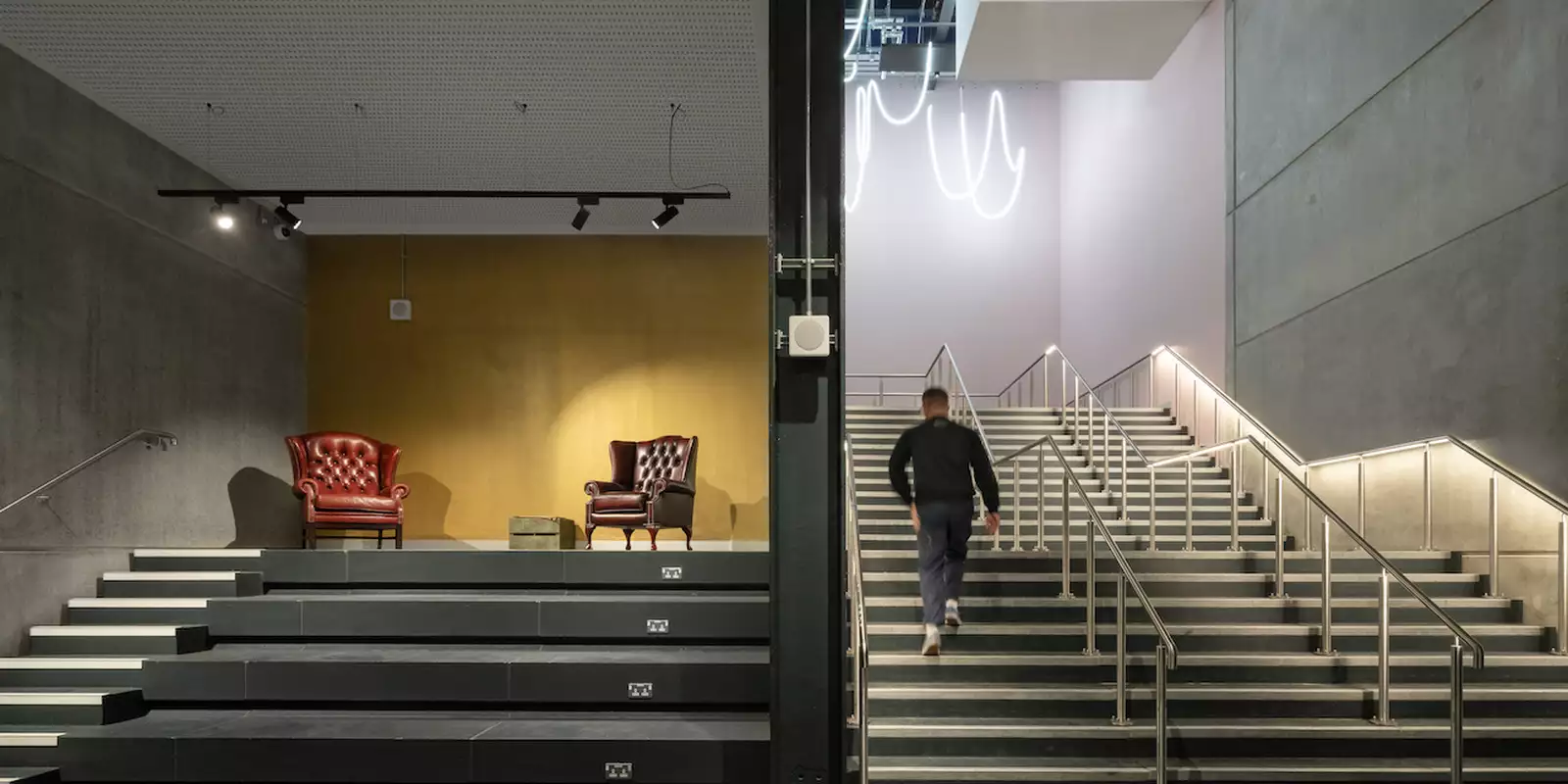 A visitor walking up the Warehouse staircase next to a stage with two armchairs on