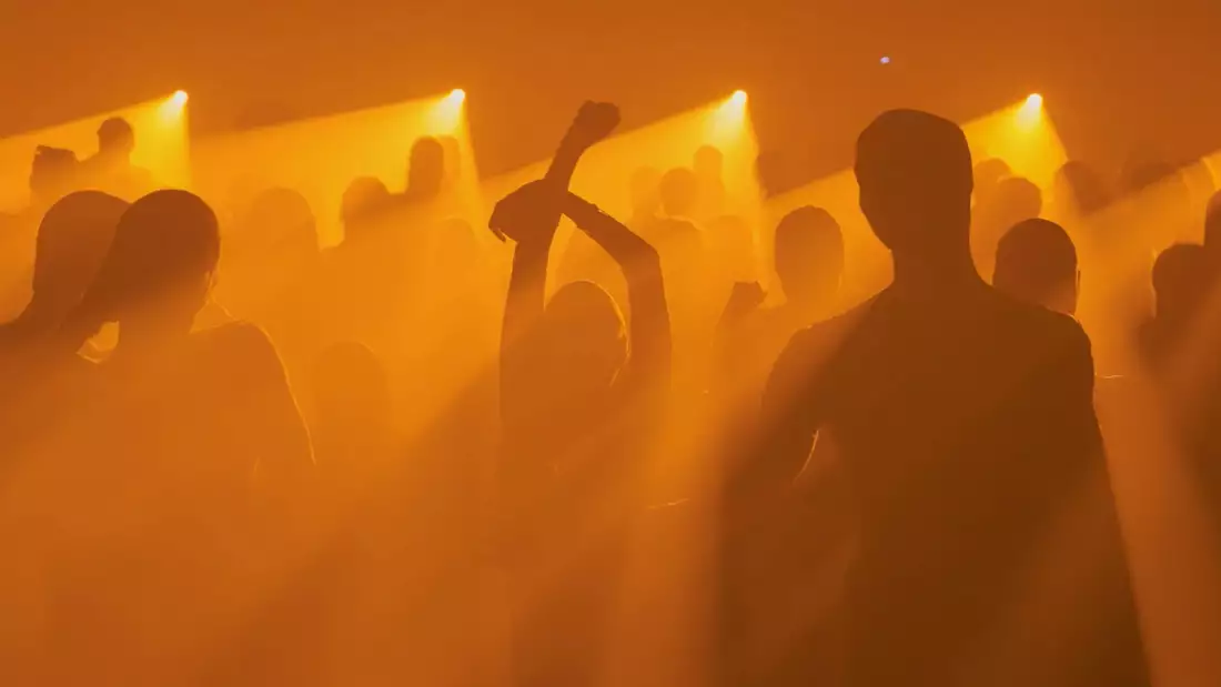 A crowd silhouetted dancing at an event bathed in orange light