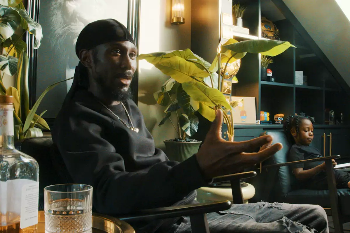 Cephas Williams sat on a chair talking surrounded by plants. His child is next to him.