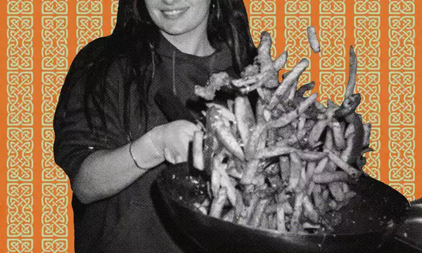 Person holding a large wok against a patterned orange background.