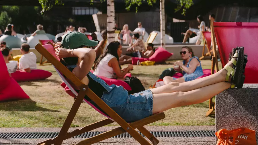 A person relaxing on a pink deck chair on grass outside Aviva Studios